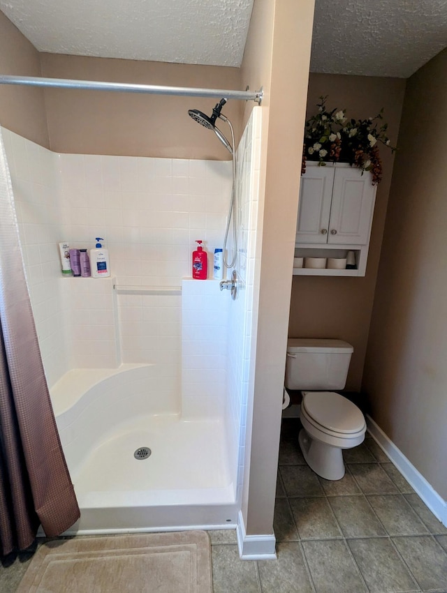 bathroom featuring a shower stall, tile patterned flooring, toilet, baseboards, and a textured ceiling