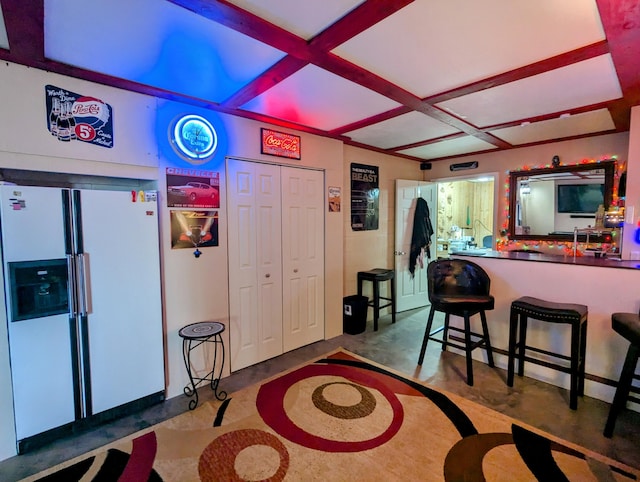 kitchen featuring a breakfast bar, white fridge with ice dispenser, and coffered ceiling
