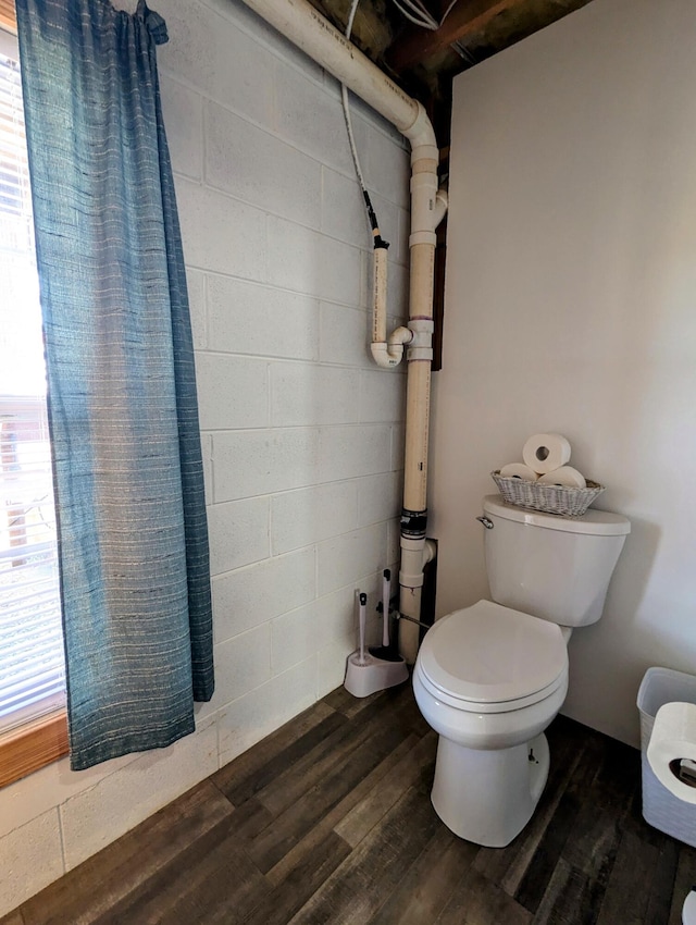 bathroom with toilet, wood finished floors, and concrete block wall