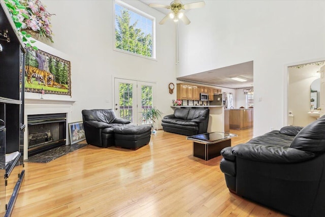 living area with a ceiling fan, a healthy amount of sunlight, a towering ceiling, and light wood-style floors