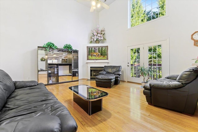 living room featuring a fireplace with flush hearth, wood finished floors, a high ceiling, and a ceiling fan