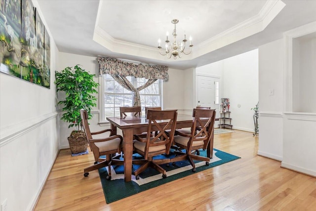 dining space featuring crown molding, light wood-type flooring, a raised ceiling, baseboards, and a notable chandelier