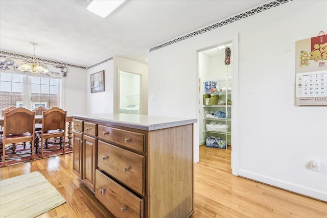 kitchen with light countertops, a kitchen island, pendant lighting, light wood-style flooring, and a notable chandelier