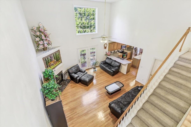 living area with french doors, light wood-style floors, a high ceiling, stairs, and ceiling fan