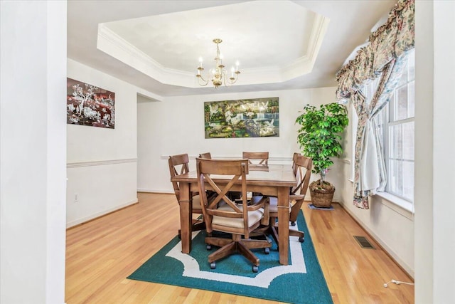 dining space featuring an inviting chandelier, a raised ceiling, wood finished floors, visible vents, and ornamental molding