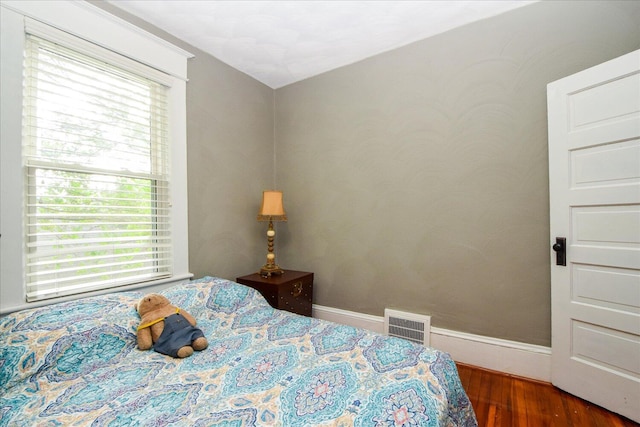 bedroom featuring baseboards, wood finished floors, visible vents, and multiple windows