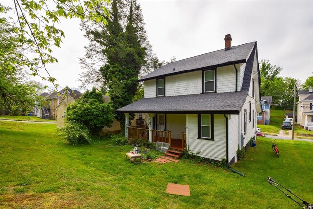 back of property with a lawn, a shingled roof, a chimney, and covered porch