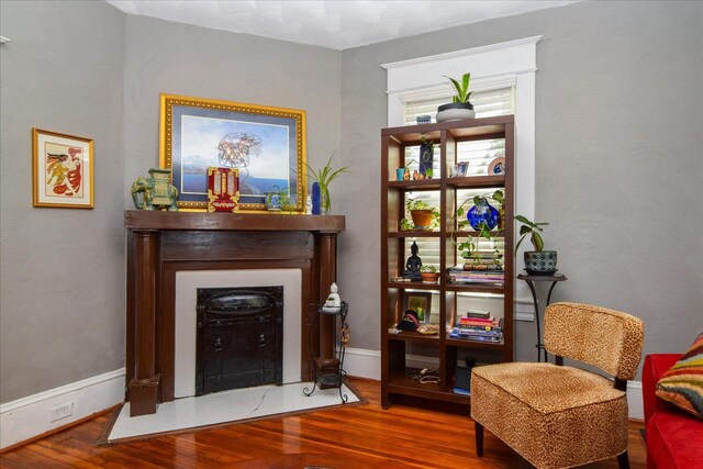 sitting room featuring a fireplace with flush hearth, baseboards, and wood finished floors