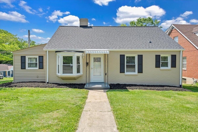bungalow-style house with a chimney, roof with shingles, a front yard, and brick siding