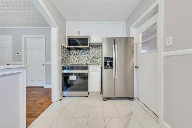 kitchen featuring tasteful backsplash, marble finish floor, light countertops, white cabinets, and appliances with stainless steel finishes