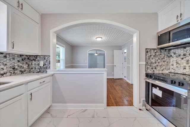 kitchen featuring stove, marble finish floor, stainless steel microwave, arched walkways, and white cabinetry