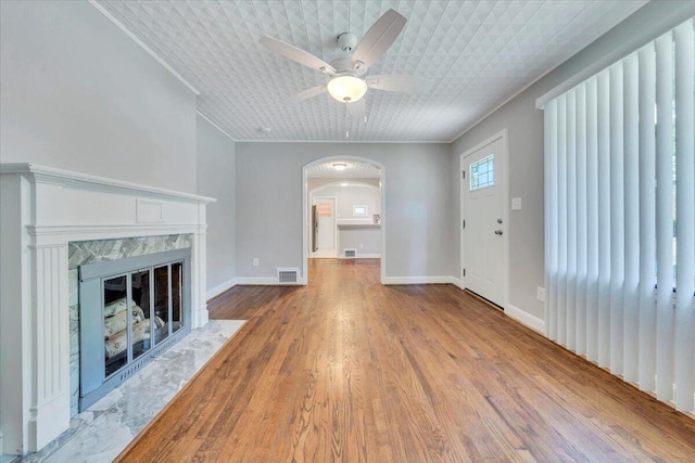unfurnished living room with a high end fireplace, visible vents, ornamental molding, arched walkways, and ceiling fan