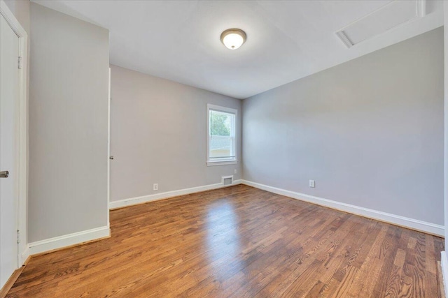 empty room featuring attic access, baseboards, wood finished floors, and visible vents