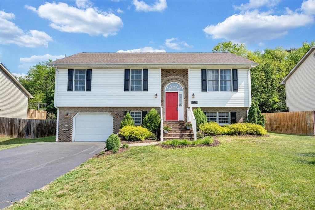 raised ranch with brick siding, fence, a front lawn, and aphalt driveway