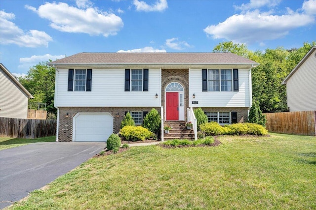 raised ranch with brick siding, fence, a front lawn, and aphalt driveway
