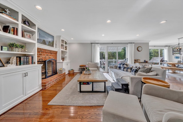 living area with crown molding, a brick fireplace, built in shelves, wood finished floors, and recessed lighting
