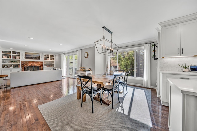 dining space with a brick fireplace, dark wood-style floors, an inviting chandelier, ornamental molding, and recessed lighting