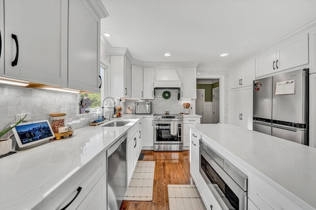 kitchen featuring wood finished floors, a sink, light stone counters, white cabinets, and stainless steel appliances