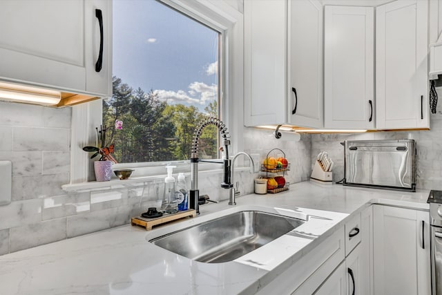 kitchen featuring a sink, light stone counters, backsplash, and white cabinetry