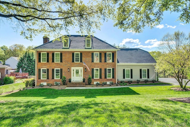 view of front of home featuring entry steps, a chimney, a front lawn, and brick siding