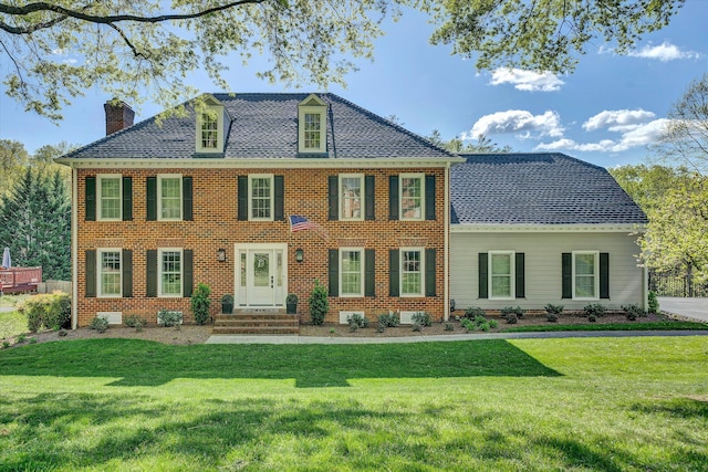 view of front of home featuring brick siding, a chimney, roof with shingles, and a front lawn