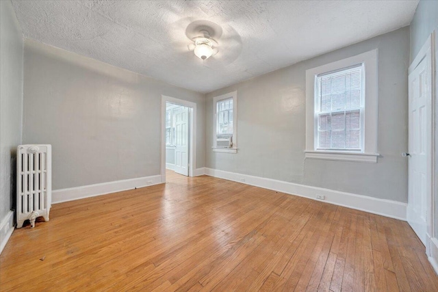 empty room featuring light wood-style flooring, a textured ceiling, baseboards, and radiator heating unit