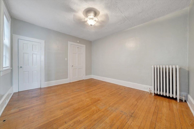 spare room with baseboards, radiator, light wood finished floors, and a textured ceiling
