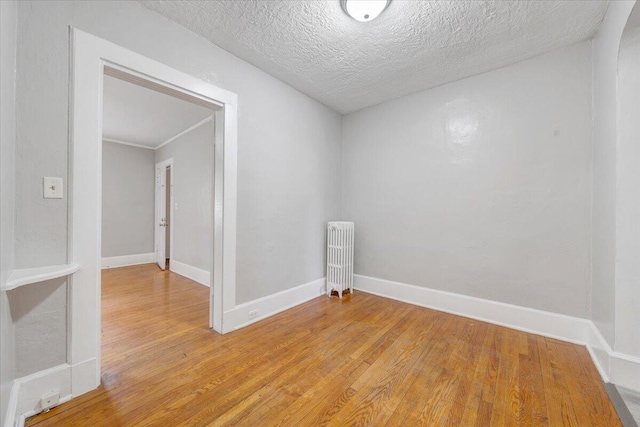 empty room featuring a textured ceiling, baseboards, radiator heating unit, and light wood-style floors