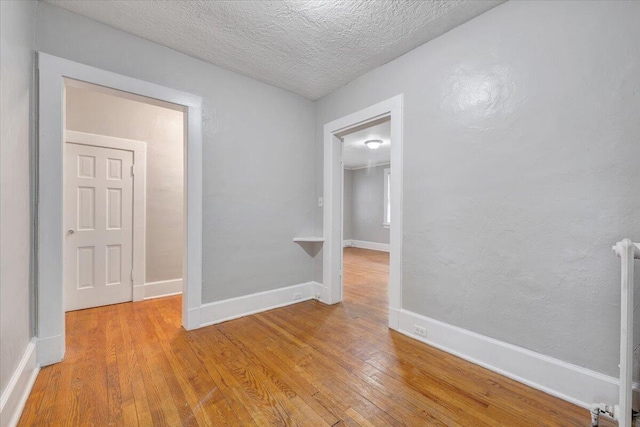 empty room with light wood-style floors, baseboards, and a textured ceiling