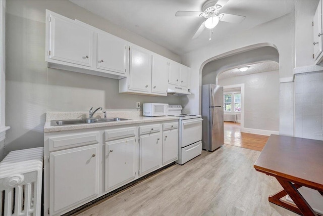 kitchen with a sink, white appliances, radiator heating unit, under cabinet range hood, and arched walkways