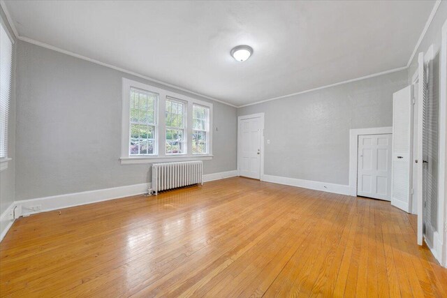 empty room with crown molding, light wood-style floors, baseboards, and radiator heating unit