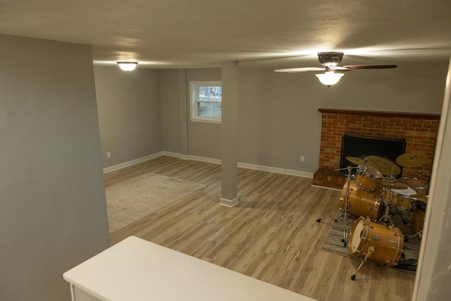 below grade area with light wood-style floors, baseboards, ceiling fan, and a fireplace