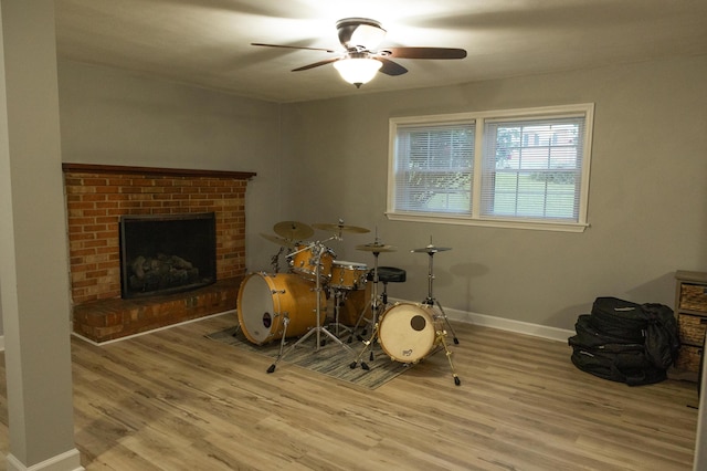 rec room with a brick fireplace, a ceiling fan, baseboards, and wood finished floors