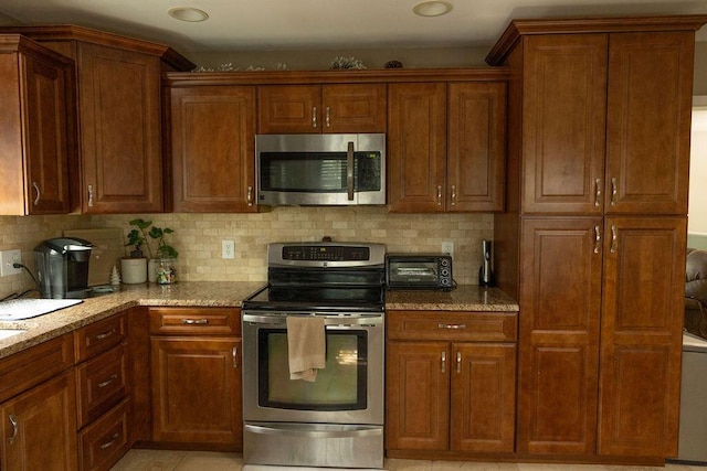 kitchen with appliances with stainless steel finishes, light stone counters, and tasteful backsplash