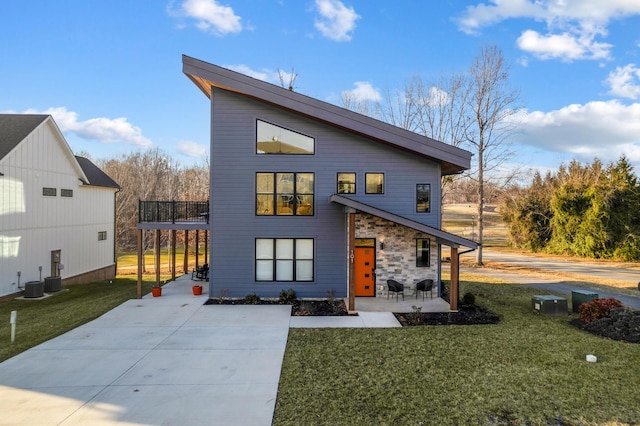 view of front of home with a balcony, concrete driveway, a front lawn, stone siding, and a patio