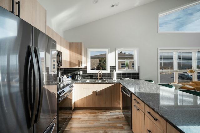 kitchen with dark stone countertops, a sink, black appliances, light wood-style floors, and visible vents