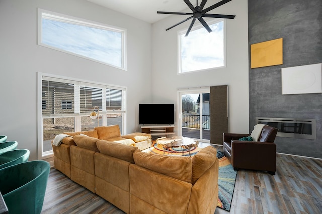 living area with a fireplace, wood finished floors, a high ceiling, and ceiling fan
