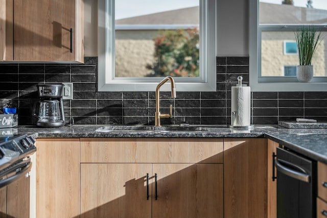 kitchen with dark stone counters, a sink, light brown cabinetry, backsplash, and stove