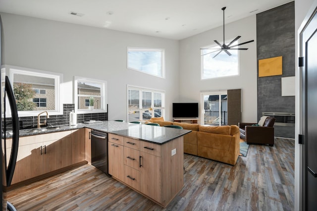 kitchen with a peninsula, stainless steel dishwasher, dark stone countertops, and wood finished floors