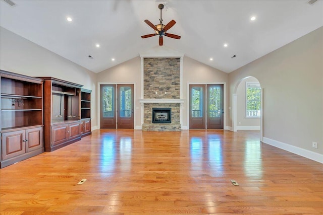 unfurnished living room featuring light wood-style floors, arched walkways, a fireplace, a ceiling fan, and high vaulted ceiling
