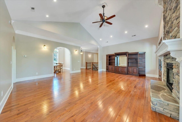 unfurnished living room featuring light wood-type flooring, arched walkways, a ceiling fan, and a stone fireplace
