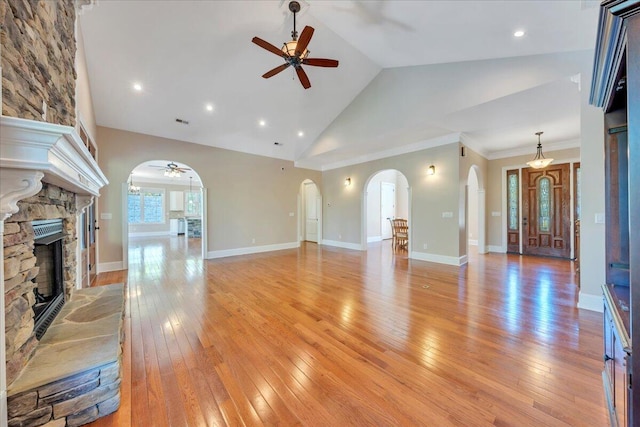 unfurnished living room with arched walkways, ceiling fan, light wood-style flooring, and a fireplace