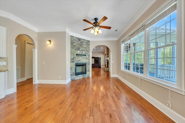 unfurnished living room featuring light wood-style flooring, visible vents, ornamental molding, a ceiling fan, and a stone fireplace