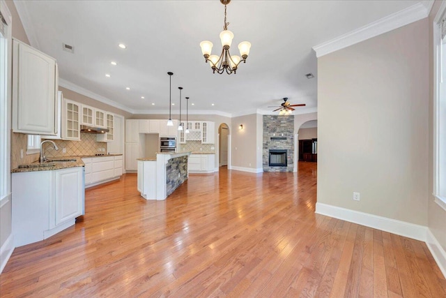 kitchen with arched walkways, oven, ceiling fan with notable chandelier, backsplash, and a sink