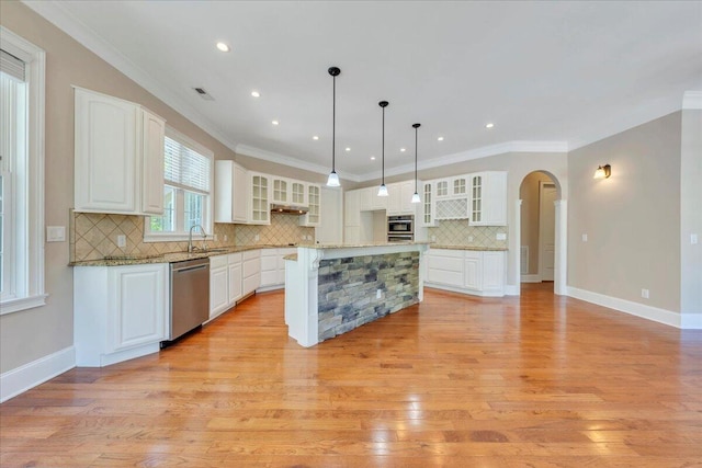 kitchen featuring arched walkways, stainless steel dishwasher, light wood-style floors, a kitchen island, and backsplash