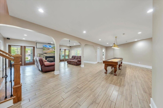 playroom featuring light wood-style floors, recessed lighting, a stone fireplace, and arched walkways