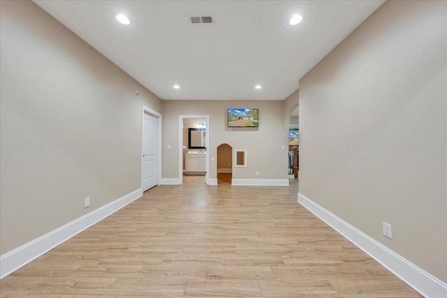 interior space featuring arched walkways, visible vents, light wood-style flooring, and baseboards