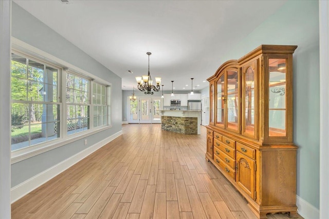 unfurnished dining area with a chandelier, baseboards, and light wood-style floors
