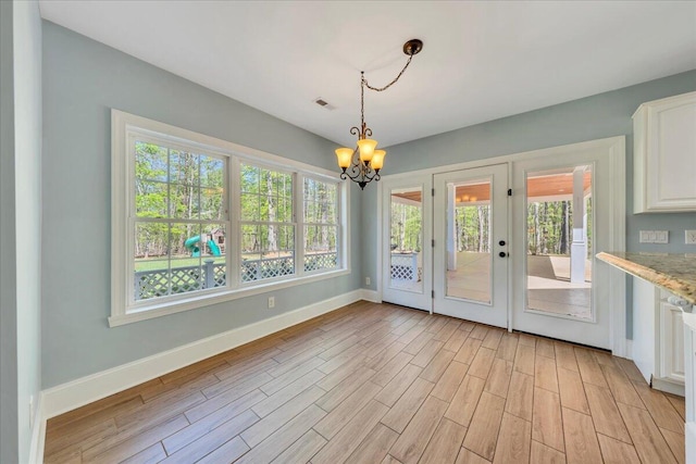 unfurnished dining area with a chandelier, light wood-style floors, visible vents, and baseboards