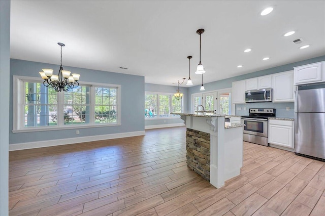 kitchen with baseboards, stainless steel appliances, an inviting chandelier, and light wood finished floors